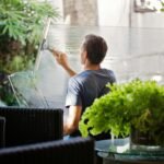 Man in Gray Shirt Cleaning Clear Glass Wall Near Sofa